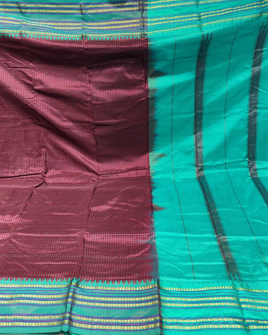 A folded and draped silk saree with a deep maroon body and a bright teal-green border, featuring black vertical stripes and gold and green woven stripes along the pallu.