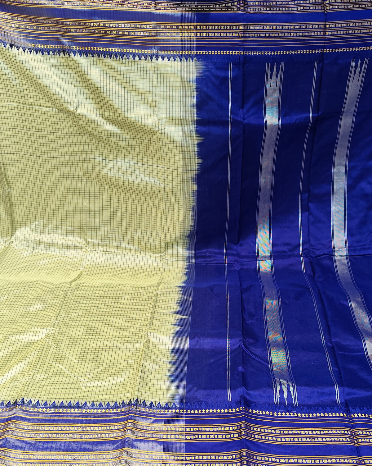 A blue and beige silk saree with intricate metallic zari patterns, displayed flat in a fabric store.