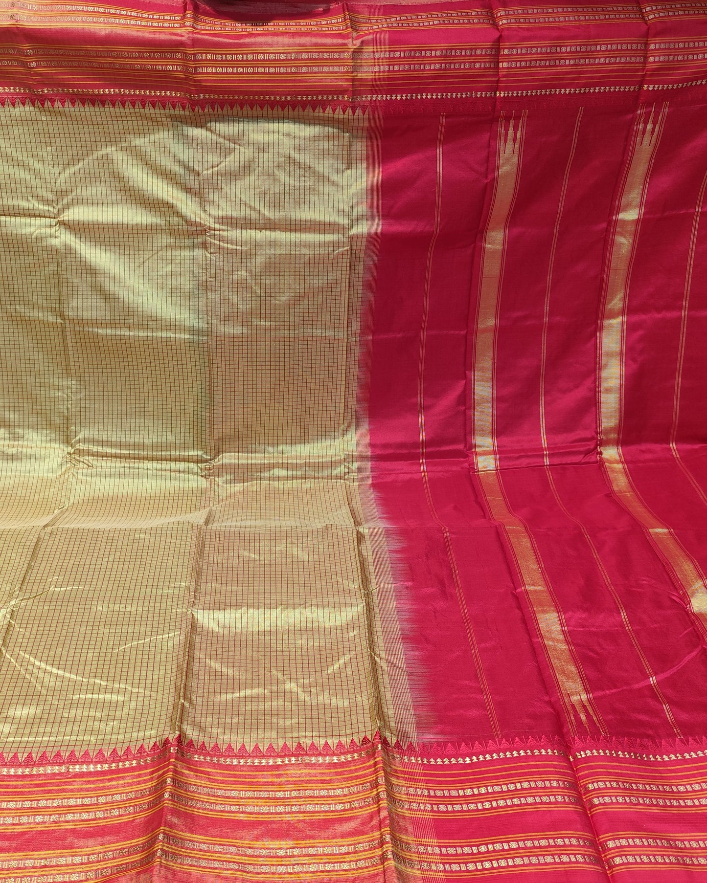 A folded and draped silk saree with a golden-beige body, a bright red border, and intricate gold zari stripes, displayed against a dark background.