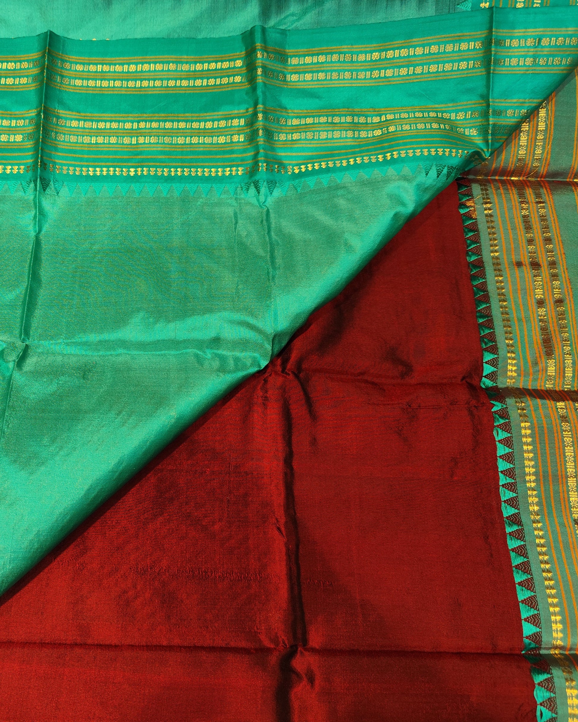 A folded Narayanpeth Maroon & Blue Saree 1silk saree fabric with a vibrant green body, a deep red underlayer, and a yellow-gold zari patterned border.