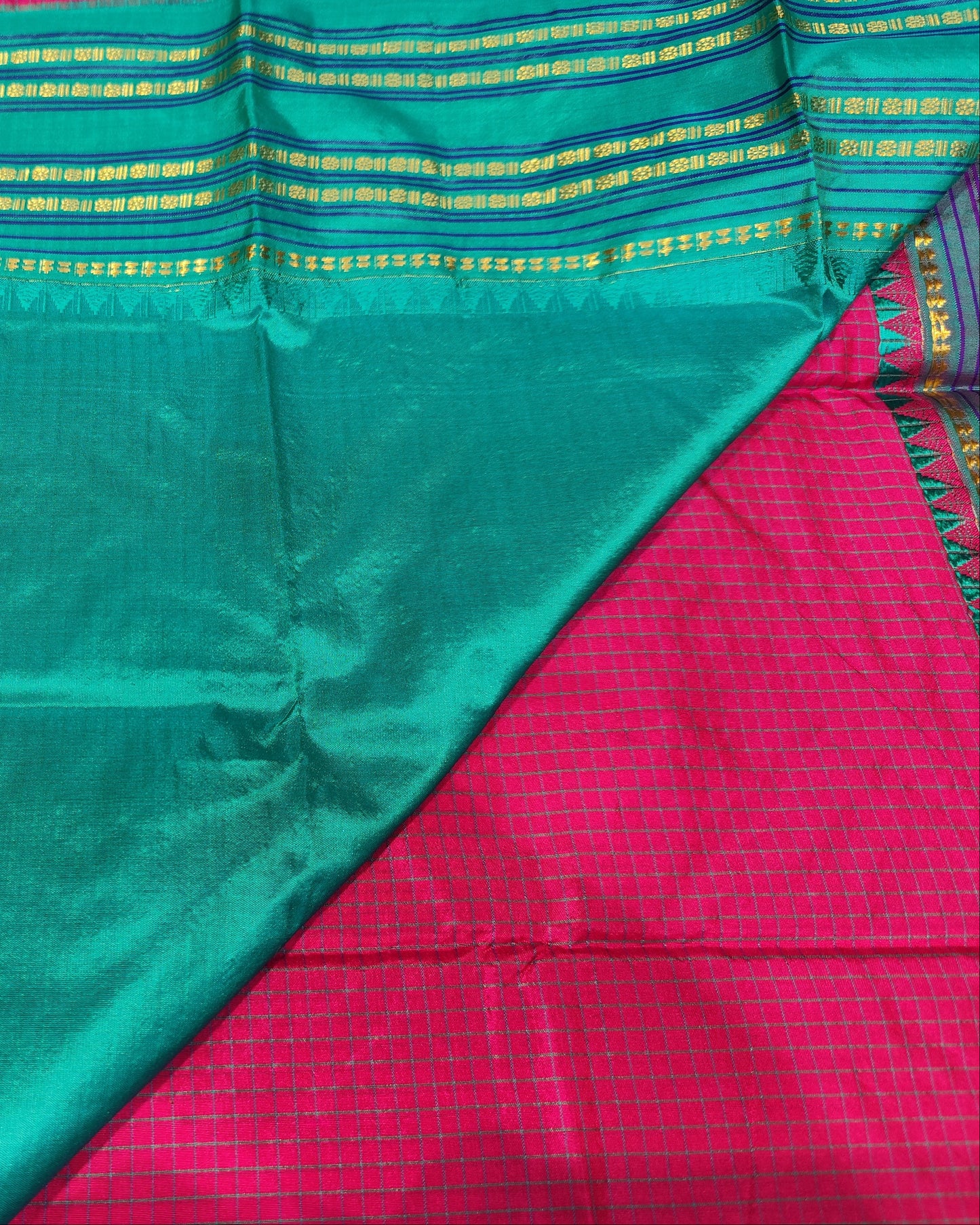 A close-up of a folded and draped Narayanpeth Saree Checks Pink saree  showing a dominant teal-green body with a border of gold and blue stripes, laid over a bright pink fabric.