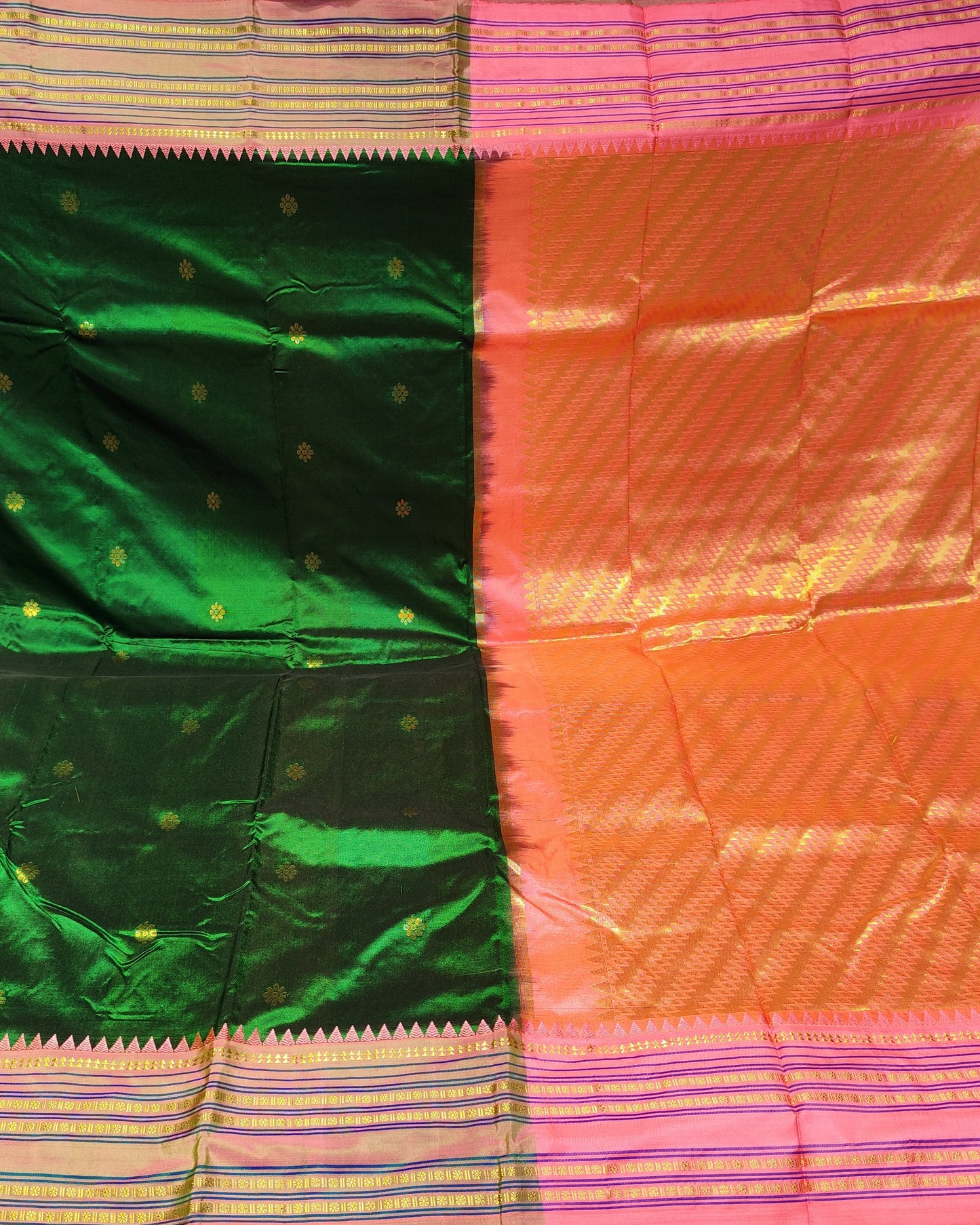 A folded and draped silk saree with a split design of emerald green and bright orange-pink, featuring gold zari motifs and borders, displayed in what appears to be a fabric store.