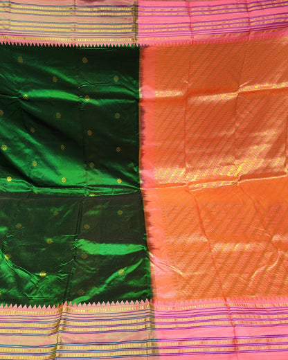A folded and draped silk saree with a split design of emerald green and bright orange-pink, featuring gold zari motifs and borders, displayed in what appears to be a fabric store.