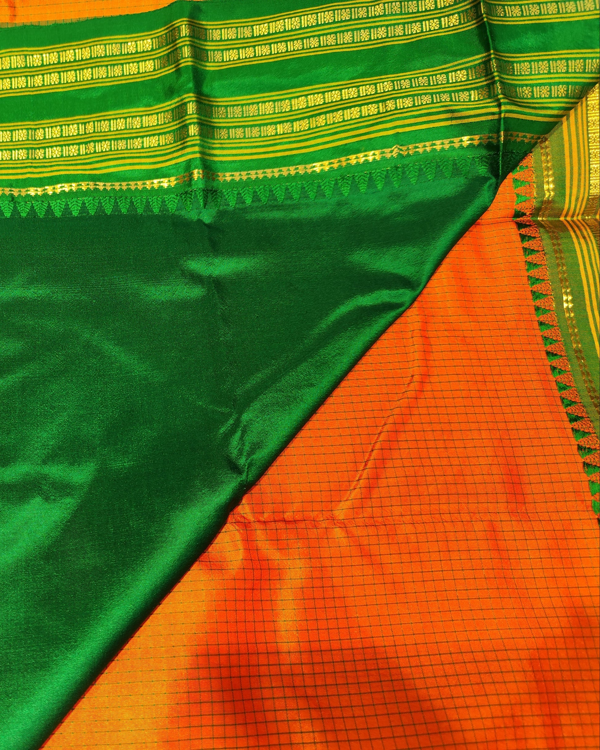 A close-up of a green and orange Narayanpeth silk saree with intricate gold zari woven borders and a geometric patterned pallu.