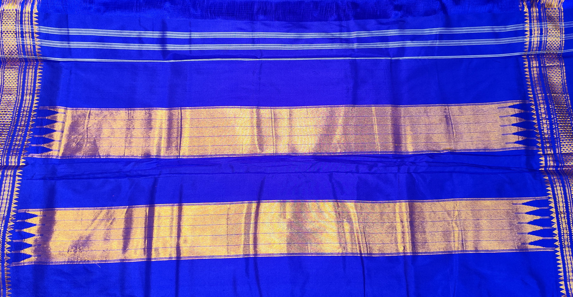 A pink and  royal blue Ilkal silk saree from karnataka with gold zari stripes and a vibrant pink border, held up by a person in a shop setting.