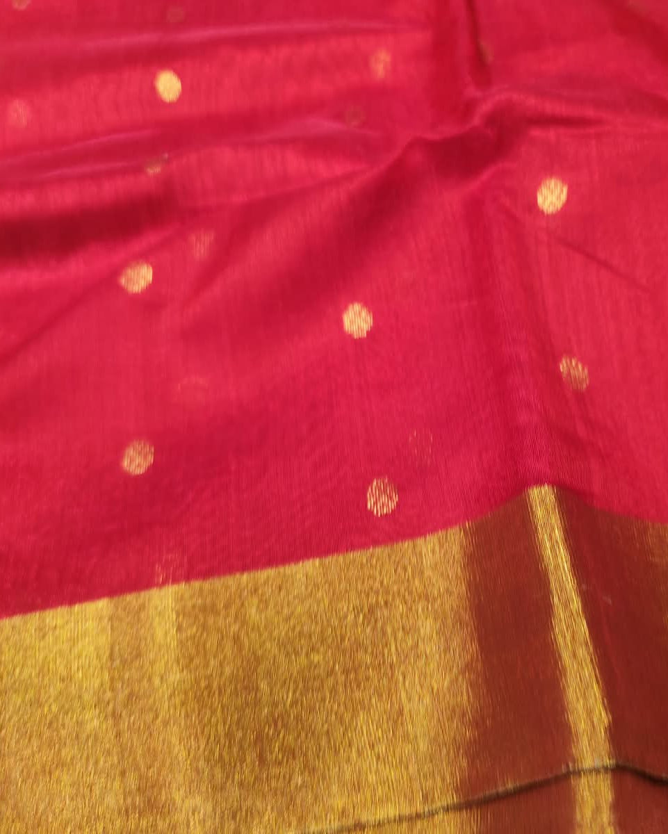A close-up of a red fabric, likely a saree, featuring small scattered gold zari motifs and a wide, richly textured gold border along the bottom edge.