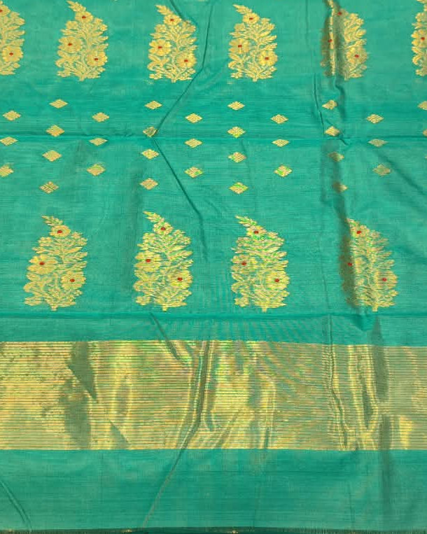 A turquoise blue and gold woven fabric, likely a saree or scarf, held up by a person in a shop setting with other folded textiles in the background.