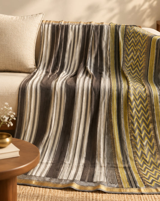 A close-up of a patterned Striped_Maheshwari_Silk_Cotton_Saree showing vertical stripes in dark brown and off-white with a decorative border featuring yellow-gold zigzag motifs and thin horizontal stripe bands.