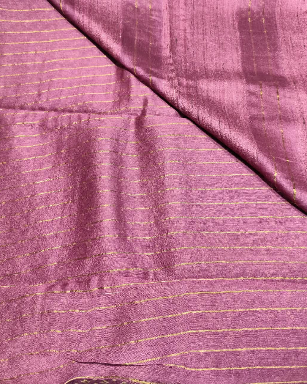 A close-up of a draped Tussar Silk & Digital Printing Pink Saree fabric with fine gold stripes and a subtle sheen.