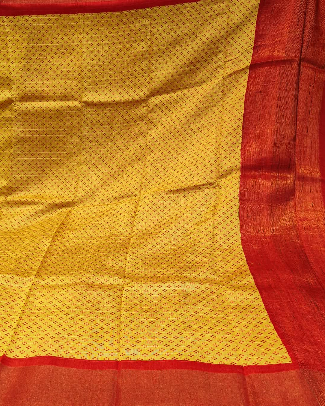 A close-up of a yellow and red woven Yellow_and_Red_Tussar_Silk_Saree_3 likely a saree or textile, featuring a yellow body with a repeating small motif and a wide red border.