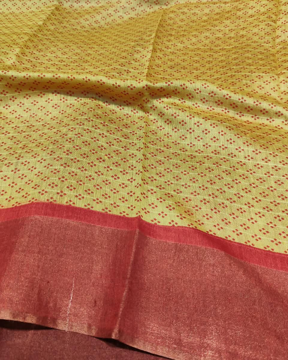 A close-up of a yellow fabric with a fine red dotted pattern and a wide rust-red border along the bottom.