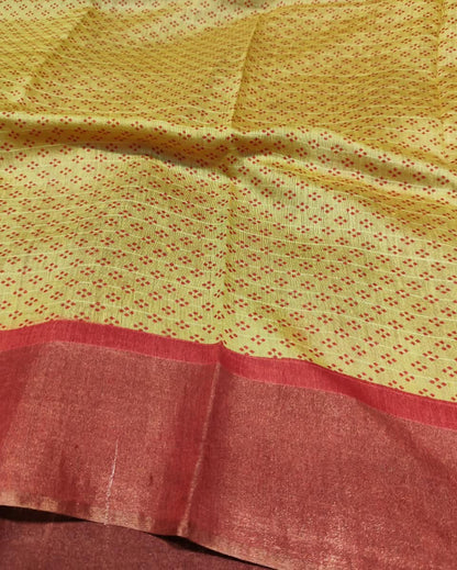 A close-up of a yellow fabric with a fine red dotted pattern and a wide rust-red border along the bottom.