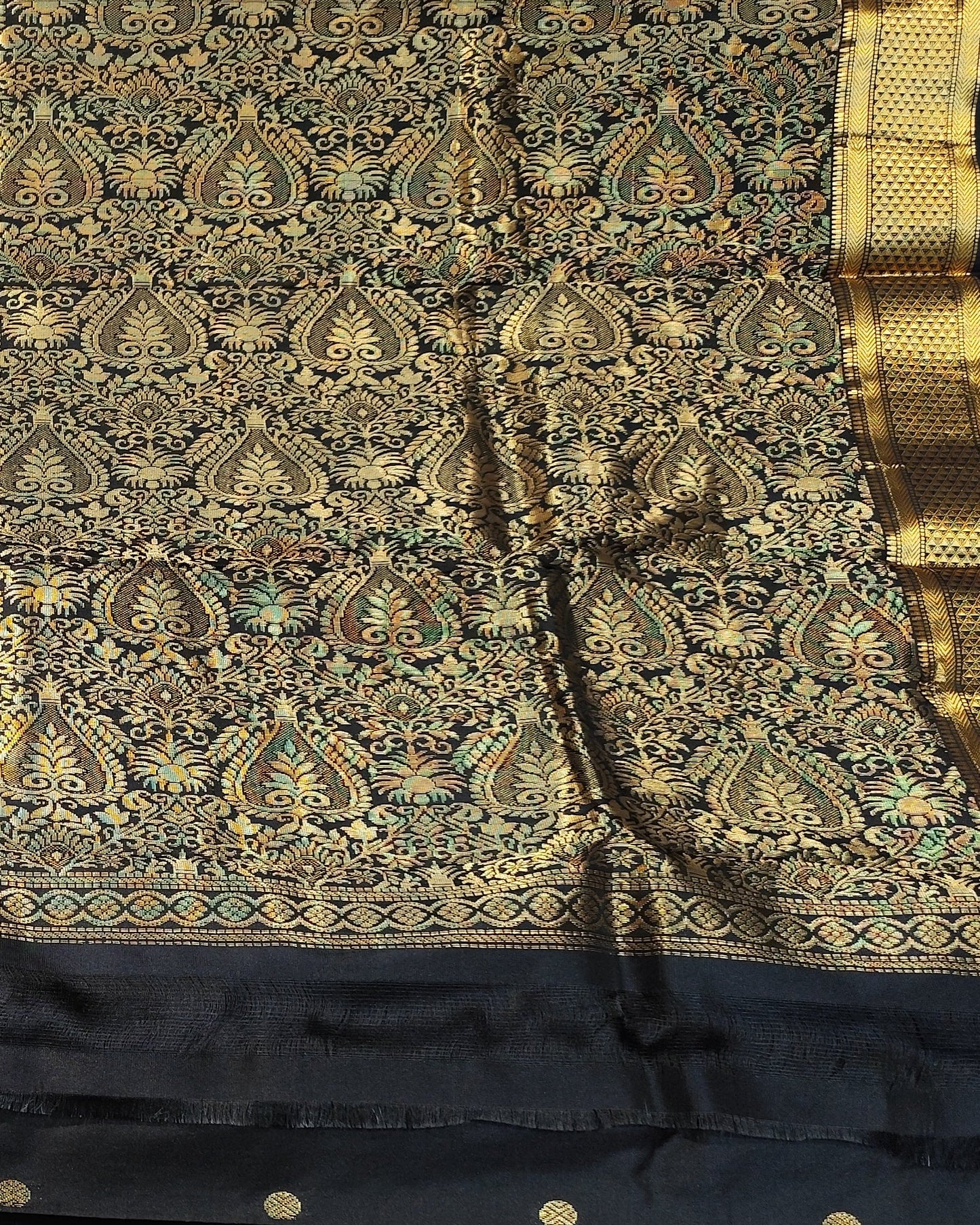 A black and gold Kanjeevaram silk. The saree features an intricate gold zari woven pattern on a black base, with a wide black border adorned with gold zari motifs and small gold buttons.