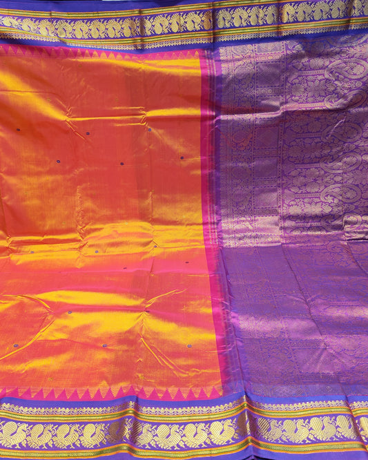 A purple and orange silk saree with intricate gold zari brocade borders, displayed flat with the pallu held out against a dark background.